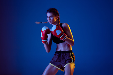 Image showing Fit caucasian woman in sportswear boxing on blue studio background in neon light