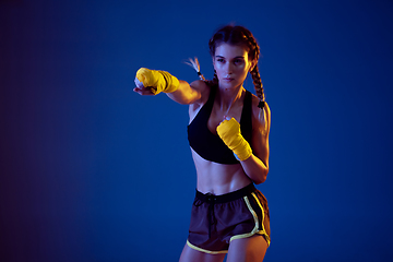 Image showing Fit caucasian woman in sportswear boxing on blue studio background in neon light