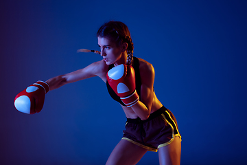 Image showing Fit caucasian woman in sportswear boxing on blue studio background in neon light