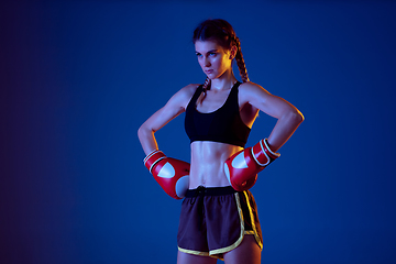 Image showing Fit caucasian woman in sportswear boxing on blue studio background in neon light