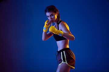 Image showing Fit caucasian woman in sportswear boxing on blue studio background in neon light