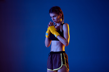 Image showing Fit caucasian woman in sportswear boxing on blue studio background in neon light