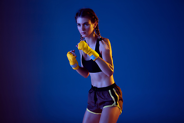 Image showing Fit caucasian woman in sportswear boxing on blue studio background in neon light