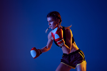 Image showing Fit caucasian woman in sportswear boxing on blue studio background in neon light
