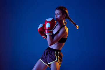 Image showing Fit caucasian woman in sportswear boxing on blue studio background in neon light