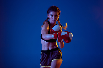 Image showing Fit caucasian woman in sportswear boxing on blue studio background in neon light