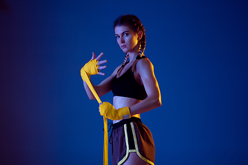 Image showing Fit caucasian woman in sportswear boxing on blue studio background in neon light