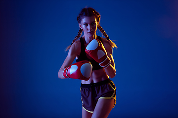 Image showing Fit caucasian woman in sportswear boxing on blue studio background in neon light