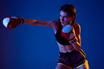 Image showing Fit caucasian woman in sportswear boxing on blue studio background in neon light