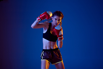 Image showing Fit caucasian woman in sportswear boxing on blue studio background in neon light