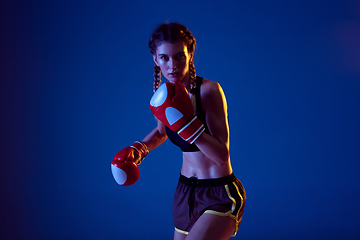 Image showing Fit caucasian woman in sportswear boxing on blue studio background in neon light