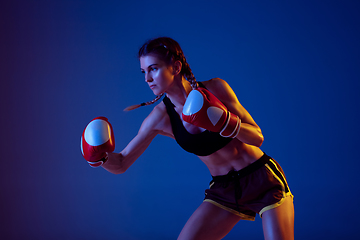 Image showing Fit caucasian woman in sportswear boxing on blue studio background in neon light