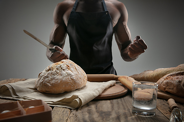 Image showing Close up of african-american man slices fresh bread with a kitchen knife