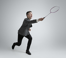 Image showing Caucasian man in office clothes plays badminton isolated on grey studio background