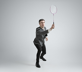 Image showing Caucasian man in office clothes plays badminton isolated on grey studio background