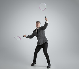 Image showing Caucasian man in office clothes plays badminton isolated on grey studio background