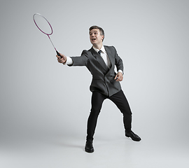 Image showing Caucasian man in office clothes plays badminton isolated on grey studio background