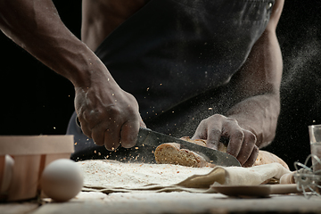 Image showing Close up of african-american man slices fresh bread with a kitchen knife