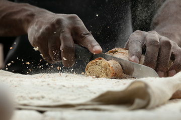 Image showing Close up of african-american man slices fresh bread with a kitchen knife