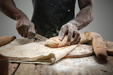 Image showing Close up of african-american man slices fresh bread with a kitchen knife