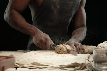 Image showing Close up of african-american man slices fresh bread with a kitchen knife