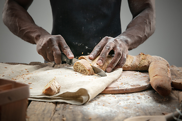 Image showing Close up of african-american man slices fresh bread with a kitchen knife