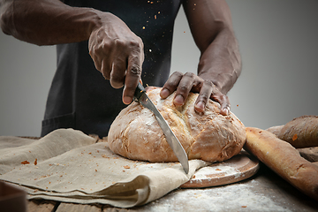 Image showing Close up of african-american man slices fresh bread with a kitchen knife