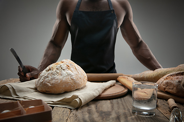 Image showing Close up of african-american man slices fresh bread with a kitchen knife