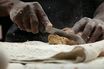 Image showing Close up of african-american man slices fresh bread with a kitchen knife