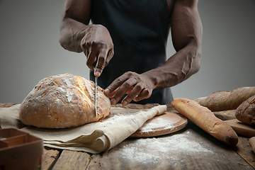 Image showing Close up of african-american man slices fresh bread with a kitchen knife