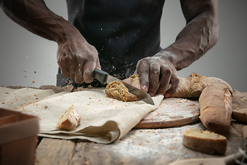 Image showing Close up of african-american man slices fresh bread with a kitchen knife