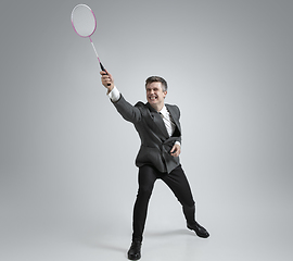 Image showing Caucasian man in office clothes plays badminton isolated on grey studio background