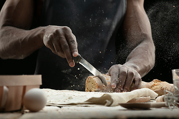 Image showing Close up of african-american man slices fresh bread with a kitchen knife