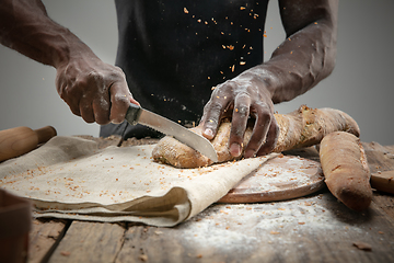 Image showing Close up of african-american man slices fresh bread with a kitchen knife