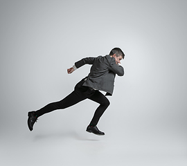 Image showing Caucasian man in office clothes running isolated on grey studio background