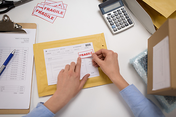 Image showing hands sticking fragile marks to parcel in envelope