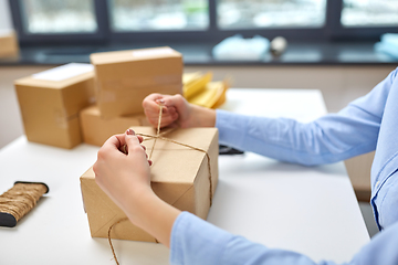 Image showing woman packing parcel and tying rope at post office