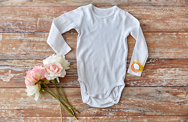 Image showing baby bodysuit with soother and flowers on wood