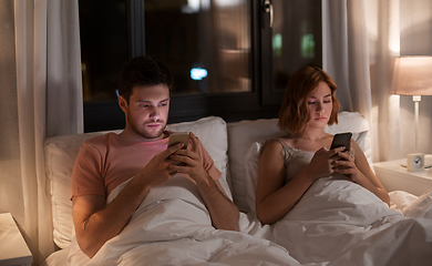 Image showing couple using smartphones in bed at night at home