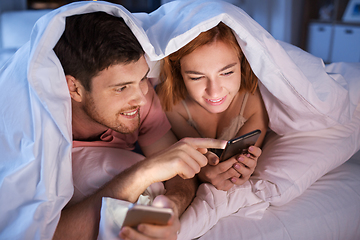 Image showing happy couple using smartphones in bed at night