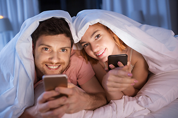 Image showing happy couple using smartphones in bed at night