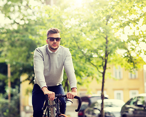 Image showing young man in shades riding bicycle on city street