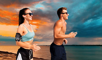 Image showing couple with phones and arm bands running on beach