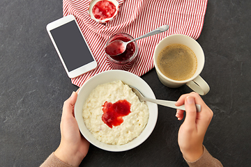 Image showing hands with porridge, jam, spoon, coffee and phone