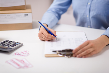 Image showing woman with clipboard and parcels at post office