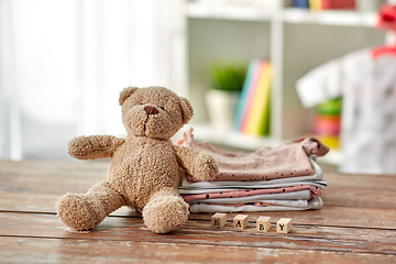 Image showing baby clothes and teddy bear toy on table at home