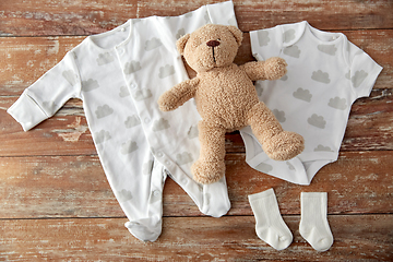 Image showing baby bodysuits and teddy bear on wooden table