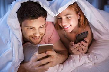 Image showing happy couple using smartphones in bed at night