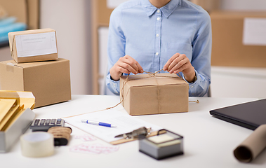 Image showing woman packing parcel and tying rope at post office