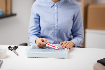 Image showing woman sticking fragile mark to wrap at post office